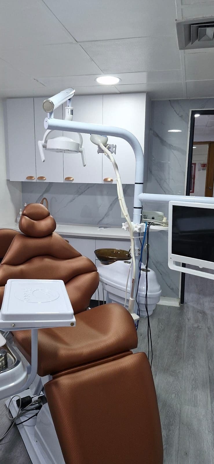 Consultorio con silla odontológica color cobre, lámpara blanca y pared de mármol claro