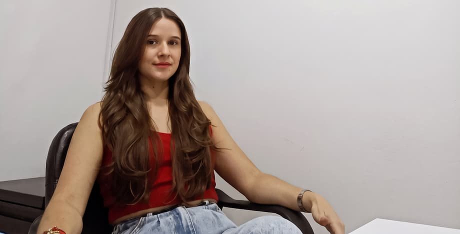 La doctora Katherynne Suárez sentada con blusa roja, esperándote en su consultorio